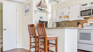 Une cuisine avec des meubles blancs, un four à micro-ondes et une cuisinière. On y trouve deux chaises en bois avec des coussins.