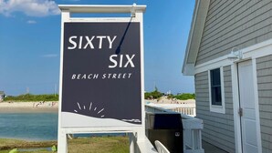 Placa à beira-mar para 'Sixty Six Beach Street', com vista para a praia e um edifício ao fundo.