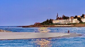 Cena costeira com uma praia, oceano e uma fileira de edifícios ao fundo.