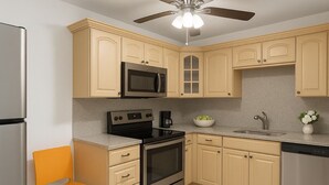 Una cocina con armarios color crema, electrodomésticos de acero inoxidable, un ventilador de techo y una lámpara.