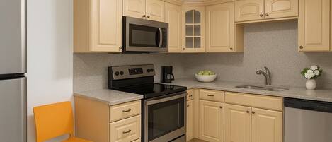 A kitchen with beige cabinets, stainless steel appliances, a ceiling fan, and a light fixture.