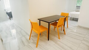 Un comedor con una mesa y cuatro sillas, una araña y vista de un dormitorio a través de un espejo.