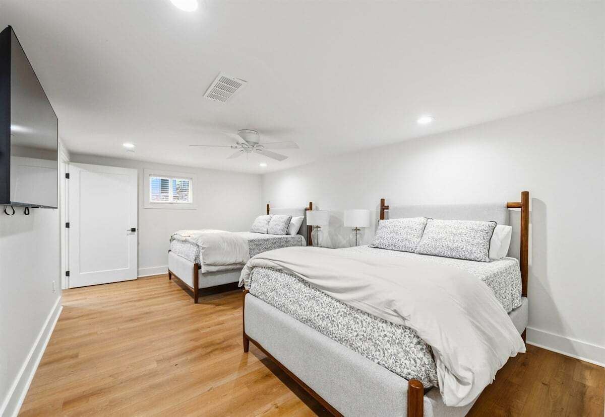 A bedroom with two beds, a ceiling fan, a TV, and a window with blinds.