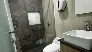 A modern bathroom with a glass-enclosed shower, a white toilet, and a wooden vanity with a sink. - HOTEL PISO 12 (Bello)