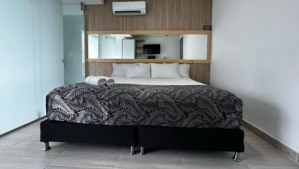 A modern hotel room with a large bed, a wooden headboard, a mirror, and a built-in air conditioning unit. - HOTEL PISO 12 (Bello)