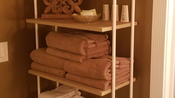 Un estante metálico blanco con varios niveles que sostiene toallas dobladas en tonos rosa y blanco.