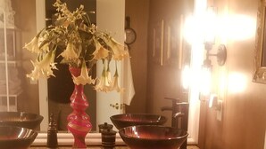 Un baño con tocador, un jarrón rosa con flores y un espejo.
