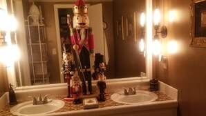 Un baño con dos lavabos, un espejo grande y una figura decorativa de soldado de hojalata en el centro.