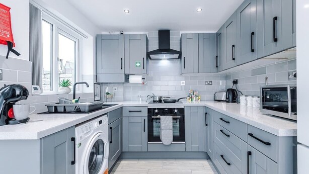 A modern kitchen with grey cabinets, a washing machine, a microwave, and a toaster. - Stylish MCR 2BR  Parking Near Etihad & Co-op (Failsworth)
