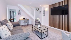 A modern living room with a sofa, coffee table, and a TV mounted on a wooden panel wall. - Stylish MCR 2BR  Parking Near Etihad & Co-op (Failsworth)