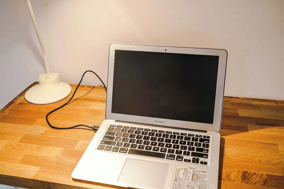 A MacBook Air laptop on a wooden table with a white power strip and cable.