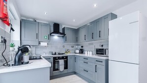 A modern kitchen with grey cabinets, a black range hood, a microwave, and a white refrigerator. - Stylish MCR 2BR  Parking Near Etihad & Co-op (Failsworth)