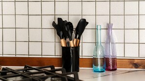 Uma bancada de cozinha com fogão a gás, um suporte para utensílios com cabos de madeira e duas garrafas decorativas.
