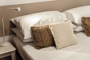 A neatly made bed with white linens and two decorative pillows, a bedside lamp, and a white nightstand. - Azalea House, in the center of Bellagio, with fitness room and private parking (bellagio)