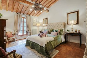 Ein Schlafzimmer mit einem großen Bett, Holzbalken, einem Chandelier, einem Fenster mit Vorhängen und einem Nachttisch mit Lampe.