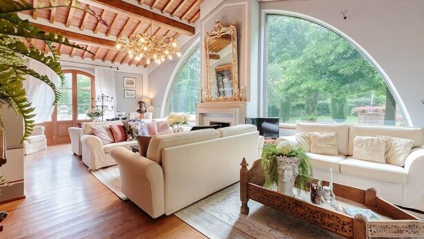 Amplia sala de estar con techo alto, chimenea y ventanas grandes que ofrecen vistas a zonas verdes.