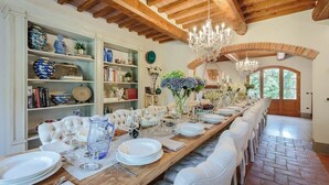 Un comedor con una larga mesa de madera dispuesta para una comida, rodeada de sillas blancas tapizadas.