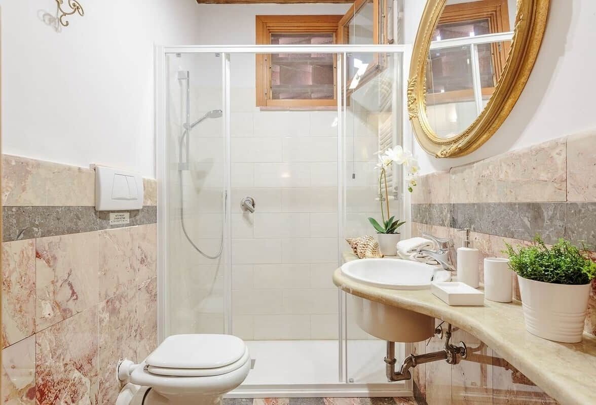 Ein Badezimmer mit Duschkabine aus Glas, einer weißen Toilette, einem Waschbecken mit Waschtisch und einem Spiegel.