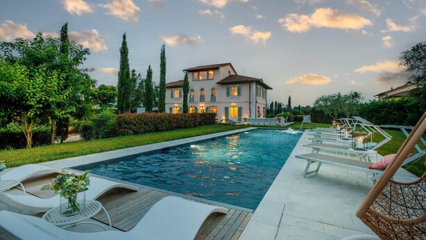 Una casa grande con piscina, sillones de descanso y un jardín bien cuidado.