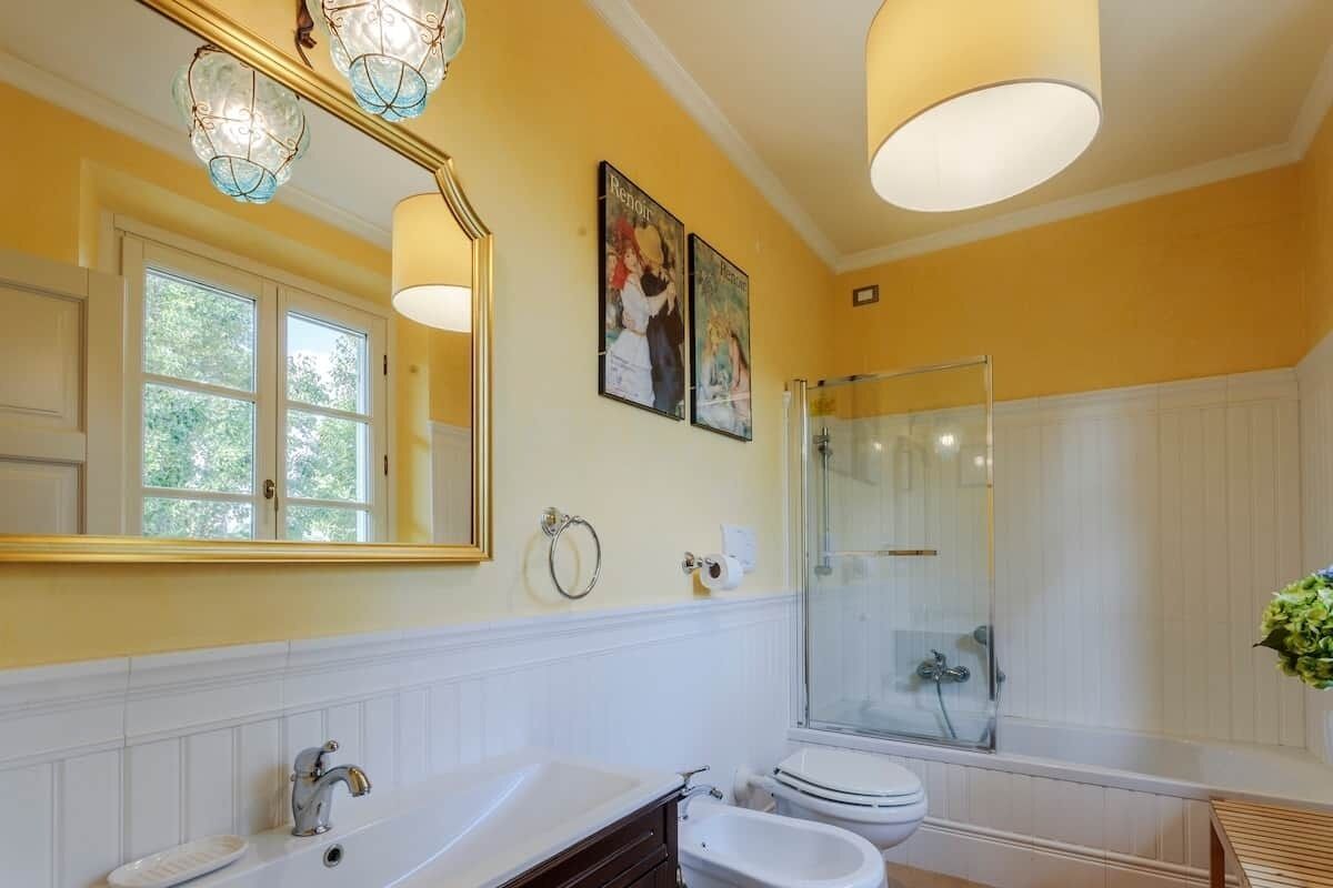 A bathroom with a large mirror, two framed pictures, a shower, and a sink.