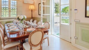 Comedor con una gran mesa de madera dispuesta para una comida, sillas, un florero y una lámpara.