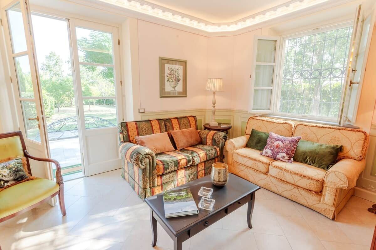A living room with two sofas, a coffee table, and a lamp. There are large windows and a door leading outside.