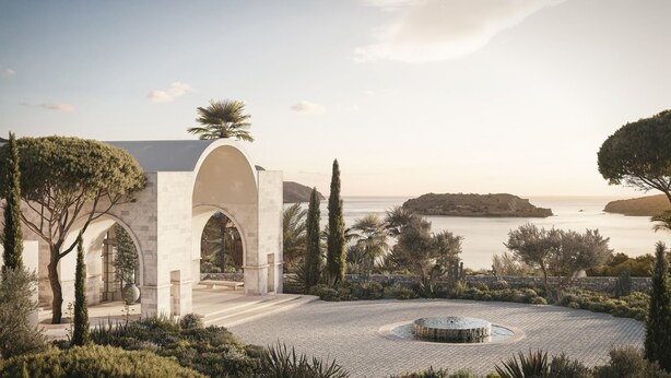 A landscaped area with a circular fountain, a stone pathway, and a view of the sea. - Rosewood Blue Palace (Agios Nikolaos)