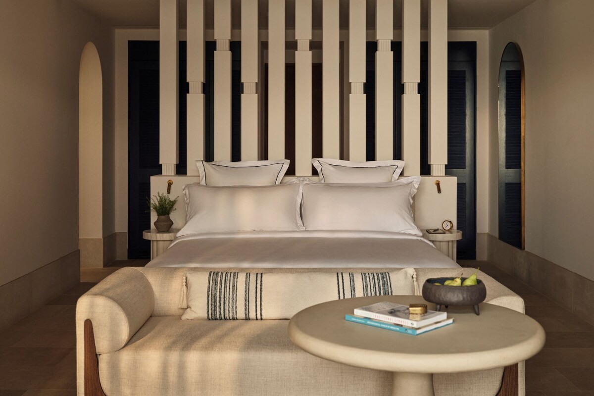 A modern bedroom with a large bed, a sofa, a round table, and a decorative wall panel.