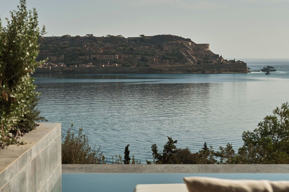 A pool with a view of a coastal town and a cliff.