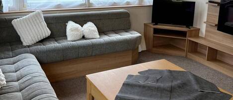 A living room with a grey sofa, a wooden coffee table, and a television on a wooden stand.