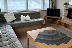 A living room with a grey sofa, a wooden coffee table, and a television on a wooden stand. - Sheena Beautiful Static Caravan Hoburne Devon Bay (Paignton)