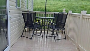 A covered outdoor area with a table and two chairs, a white fence, and a grassy lawn in the background. - Sheena Beautiful Static Caravan Hoburne Devon Bay (Paignton)