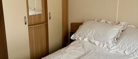 A single bed with white bedding and a wooden headboard, positioned against a plain wall with a door to the left.