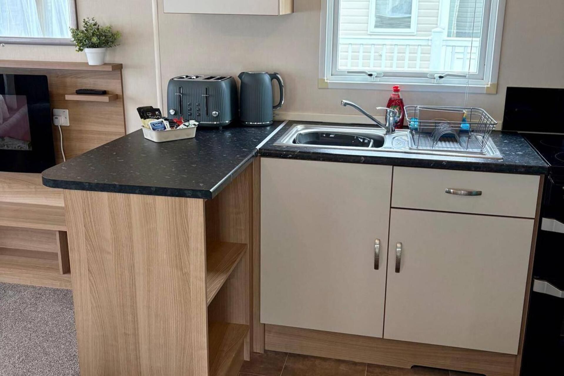 Eine kompakte Küche mit eingebautem Toaster, Wasserkocher und Spüle inklusive Geschirrgestell.