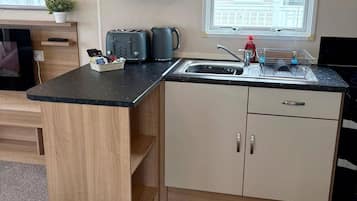 A compact kitchen with a built-in toaster, kettle, and a sink with a dish rack.