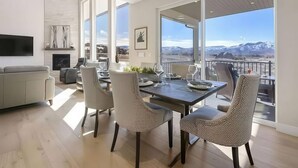 Ein stilvoller Essbereich mit großem Tisch und Stühlen, Kamin und Blick auf Berge durch bodengrosse Fenster.
