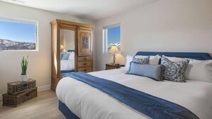 Ein Schlafzimmer mit einem großen Bett, einem Deckenventilator, einem Nachttisch mit Lampe, einem Holzschrank und einem Fenster mit Blick.