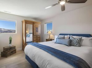 A bedroom with a large bed, a ceiling fan, a nightstand with a lamp, a wooden wardrobe, and a window with a view. - 4 BR Home - Hot Tub - Spectacular Mountain Views! (Heber City)