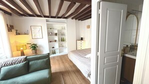 A bedroom with a bed, a bedside table, a dresser, and a nightstand. There is a window with curtains, a lamp, and a plant. - Cosy duplex in the heart of the historic center (Auxerre)