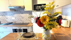 A kitchen with a dining table set for two, a vase of flowers, and a toaster. - Cosy duplex in the heart of the historic center (Auxerre)