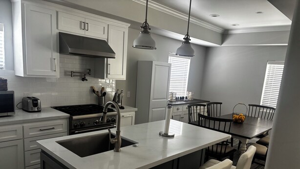 Eine moderne Küche mit einer zentralen Kochinsel, weißen Schränken, Edelstahlgeräten und Pendelleuchten.