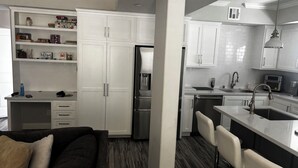 Eine moderne Küche mit weißen Schränken, einem Einbauofen, einem Kühlschrank und einem Essbereich mit Barhocker.