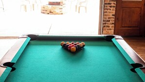 A pool table with balls in the center, a brick wall, and a door leading outside. - Woody’s Roadhouse Retreat: Barndominium Near Lake Alan Henry (Justiceburg)