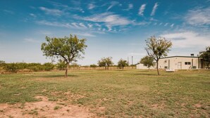 A spacious outdoor area with a building, trees, and a fence. - Woody’s Roadhouse Retreat: Barndominium Near Lake Alan Henry (Justiceburg)