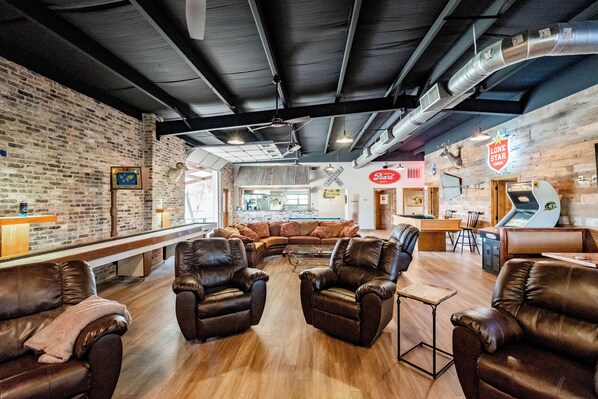 A modern lounge area with leather sofas, a pool table, and a bar area with a neon sign.