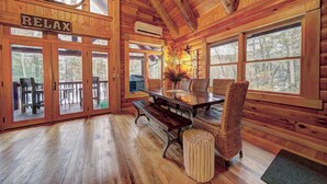 Interno di una baita in legno con un tavolo in legno, panche e un cartello con la scritta 'RELAX'.