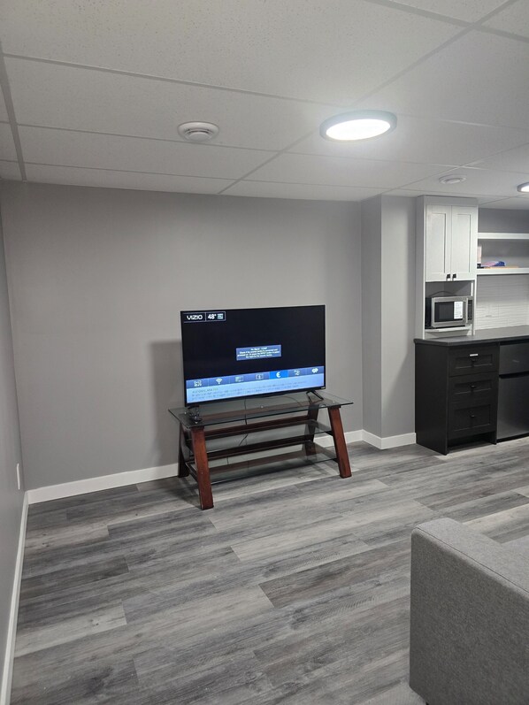 Un salón moderno con un televisor de pantalla plana sobre un mueble de vidrio, paredes grises y una alfombra gris.