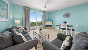 Una sala de estar con sofá, mesa de centro, televisor, comedor y balcón con cortinas.