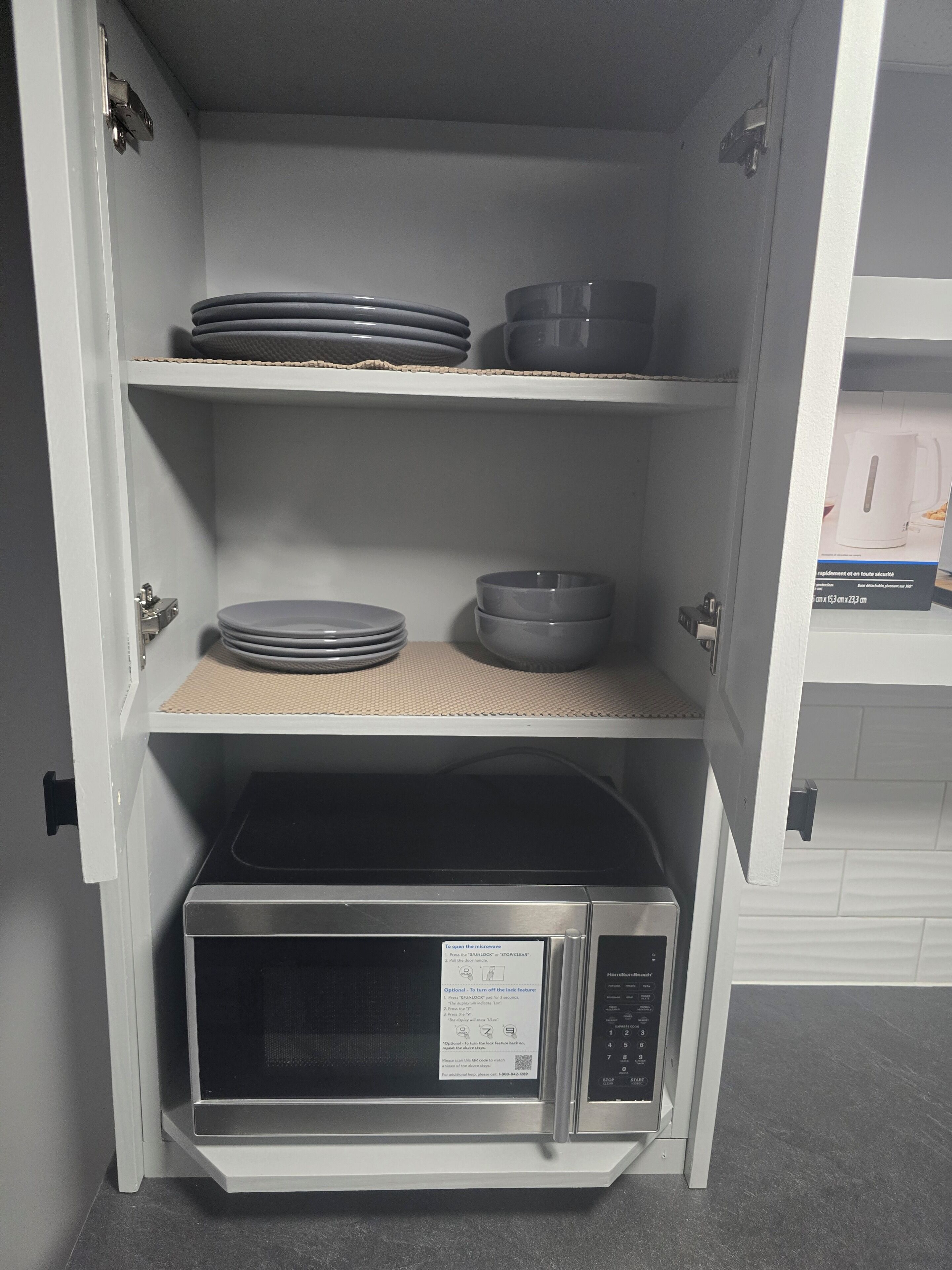 Una cocina equipada con microondas, estantes con platos, tazones y tetera.