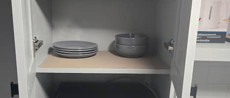 Una cocina equipada con microondas, estantes con platos, tazones y tetera.